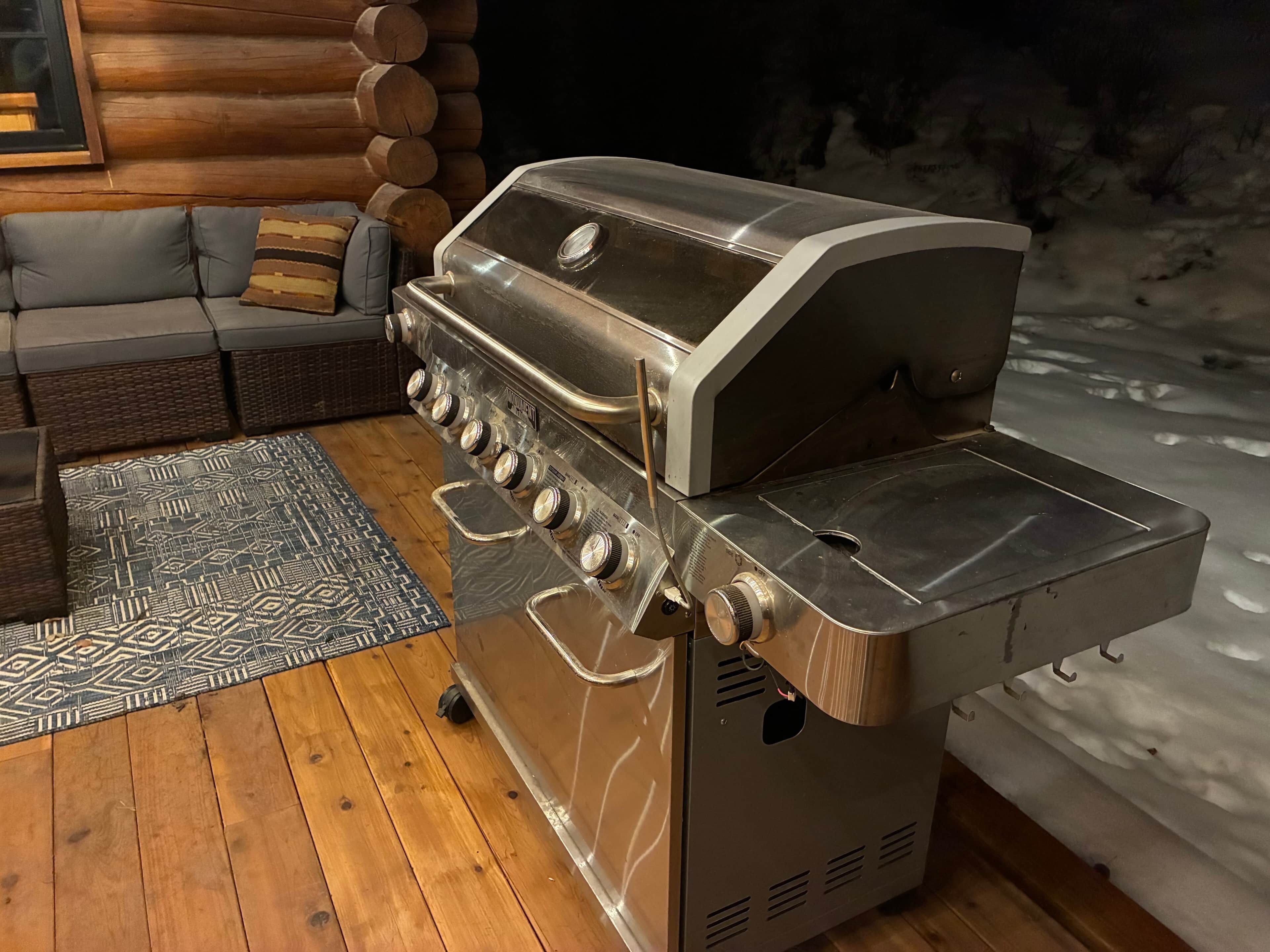 A portable stainless steel grill with a control panel, located in a cozy log cabin with a wooden floor and a patterned rug.