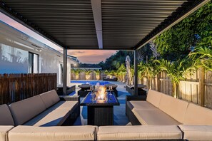Eine überdachte Terrasse im Freien mit Pool, Liegebereich und Feuerstelle.