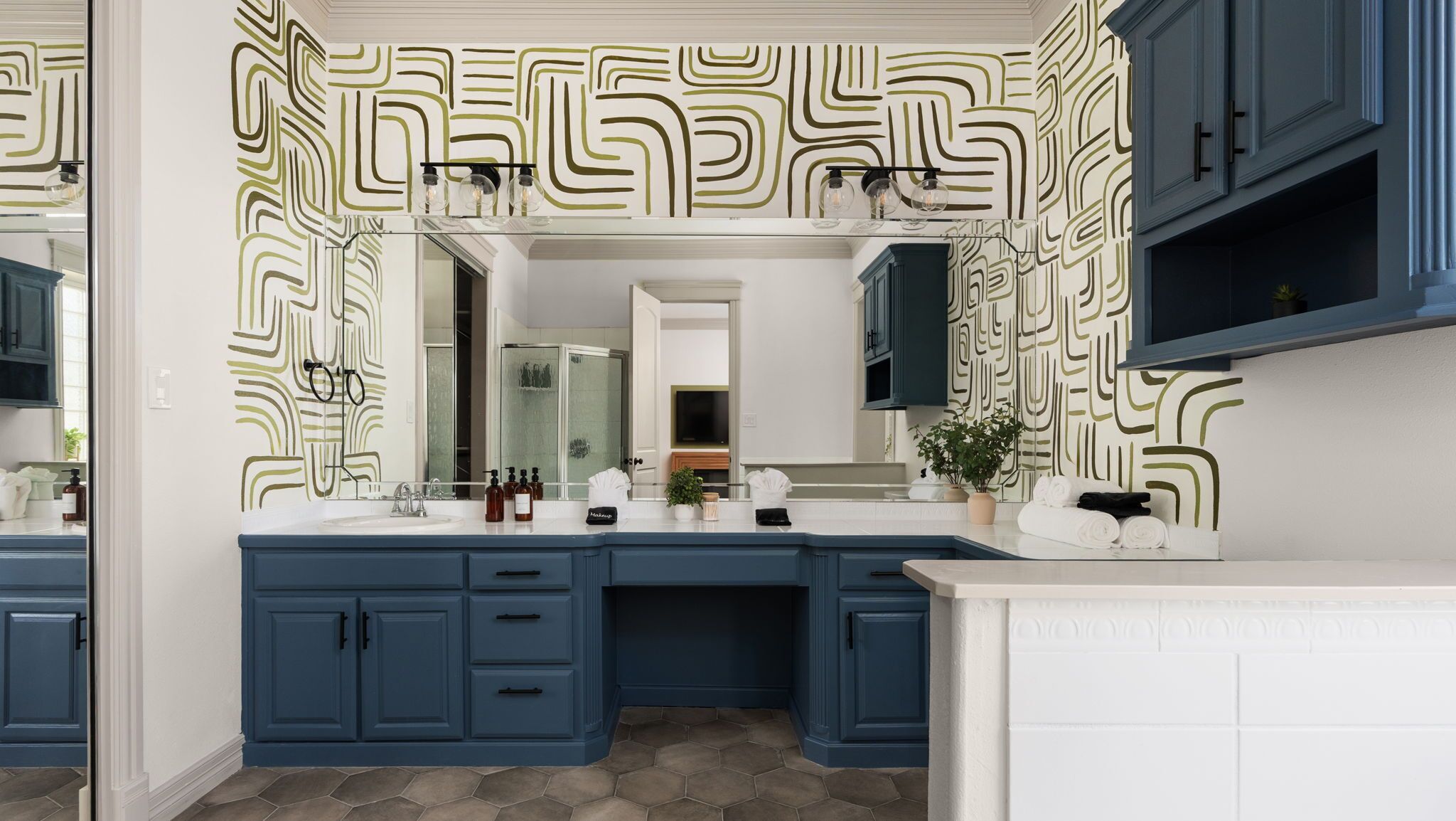 A modern bathroom with a large mirror, blue cabinets, and a patterned wall.