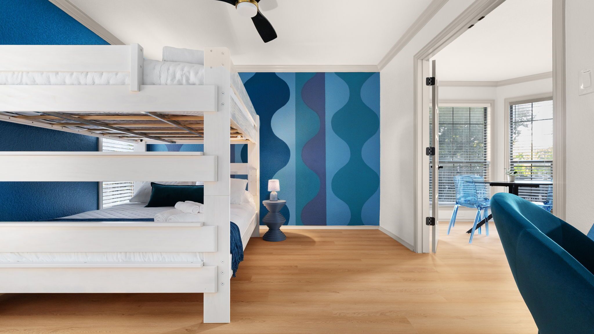 A modern room with a bunk bed, a blue patterned wall, a wooden floor, and a blue chair.