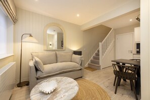A living room with a sofa, a coffee table, a floor lamp, a dining area with a table and chairs, and a staircase. - Argyl | Central Old Town Mews Home w/ Parking (Edinburgh)