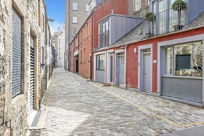 Eine enge Kopfsteinpflasterstraße mit Häusern an beiden Seiten, darunter ein roter Backsteinbau mit grauem Vordach und ein Steinhaus mit Metallvordach.