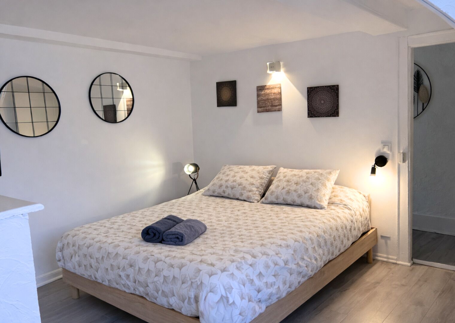 A bedroom with a bed, two wall-mounted mirrors, bedside lamps, and a small wall art piece.