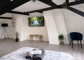 A bedroom with a bed, a bench, a TV, and a plant. - Apart'Moment EN GROUPE - La Terrasse Victor Hugo (Saint-Omer)