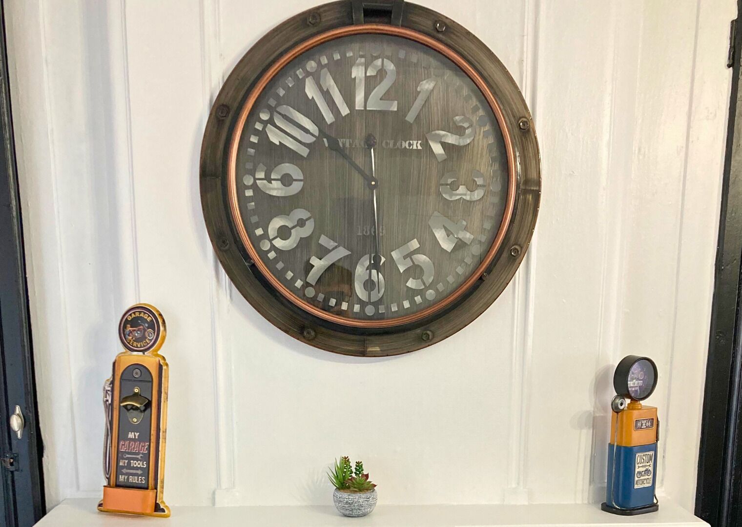 Une horloge murale au design rétro, un emblème d’atelier de réparation automobile et une petite plante en pot.