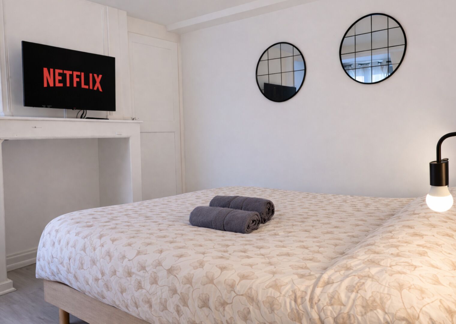 Een slaapkamer met een bed, een televisie op een standaard, twee spiegelwanden en een bedlampje.