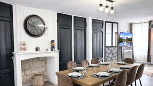 A dining room with a fireplace, a large wall clock, and a television. - Apart'Moment EN GROUPE - La Terrasse Victor Hugo (Saint-Omer)