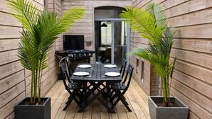 A wooden deck with a table and chairs, a grill, and potted plants. - Apart'Moment EN GROUPE - La Terrasse Victor Hugo (Saint-Omer)