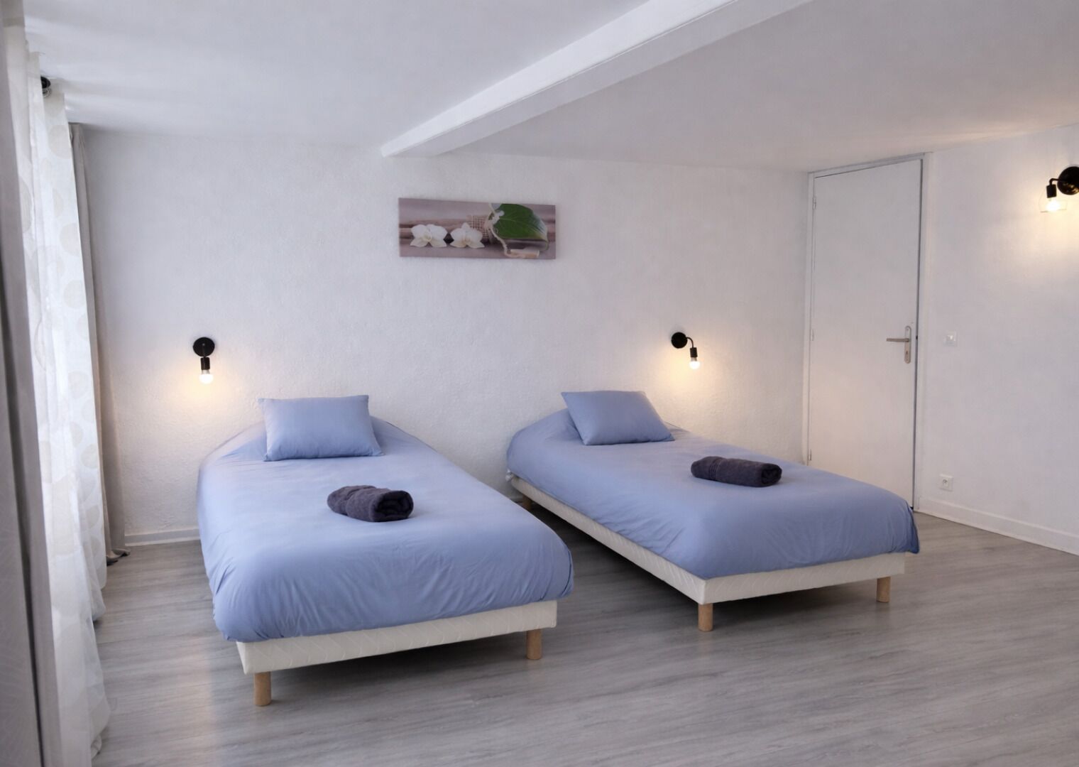 A room with two single beds, white walls, a wooden floor, and a door.