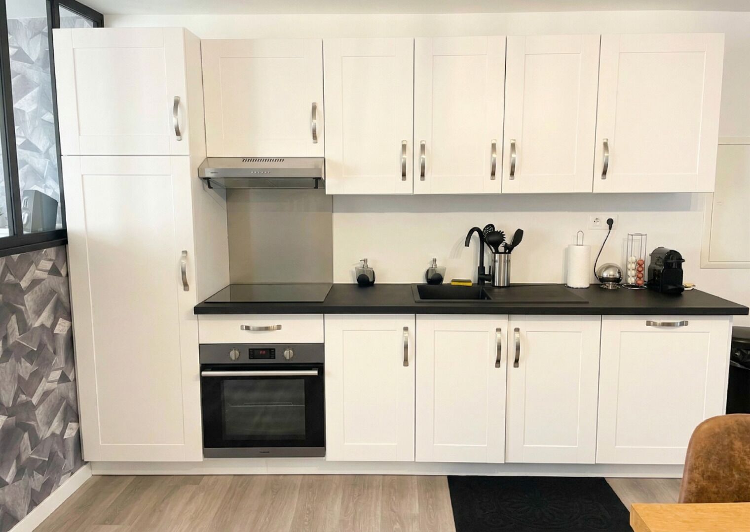 A modern kitchen with white cabinets, a black countertop, stainless steel appliances, and a built-in oven.