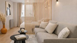 A modern living room with a grey sofa, a small round coffee table, and a decorative screen. - Montmartre studio with elevator access (Paris)