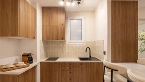 A compact kitchen with wooden cabinets, a white countertop, a sink, and a small dining area with a chair. - Montmartre studio with elevator access (Paris)