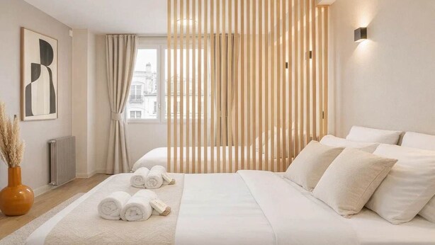 A modern hotel room with a large bed, a wooden divider, a radiator, and a city view. - Montmartre studio with elevator access (Paris)