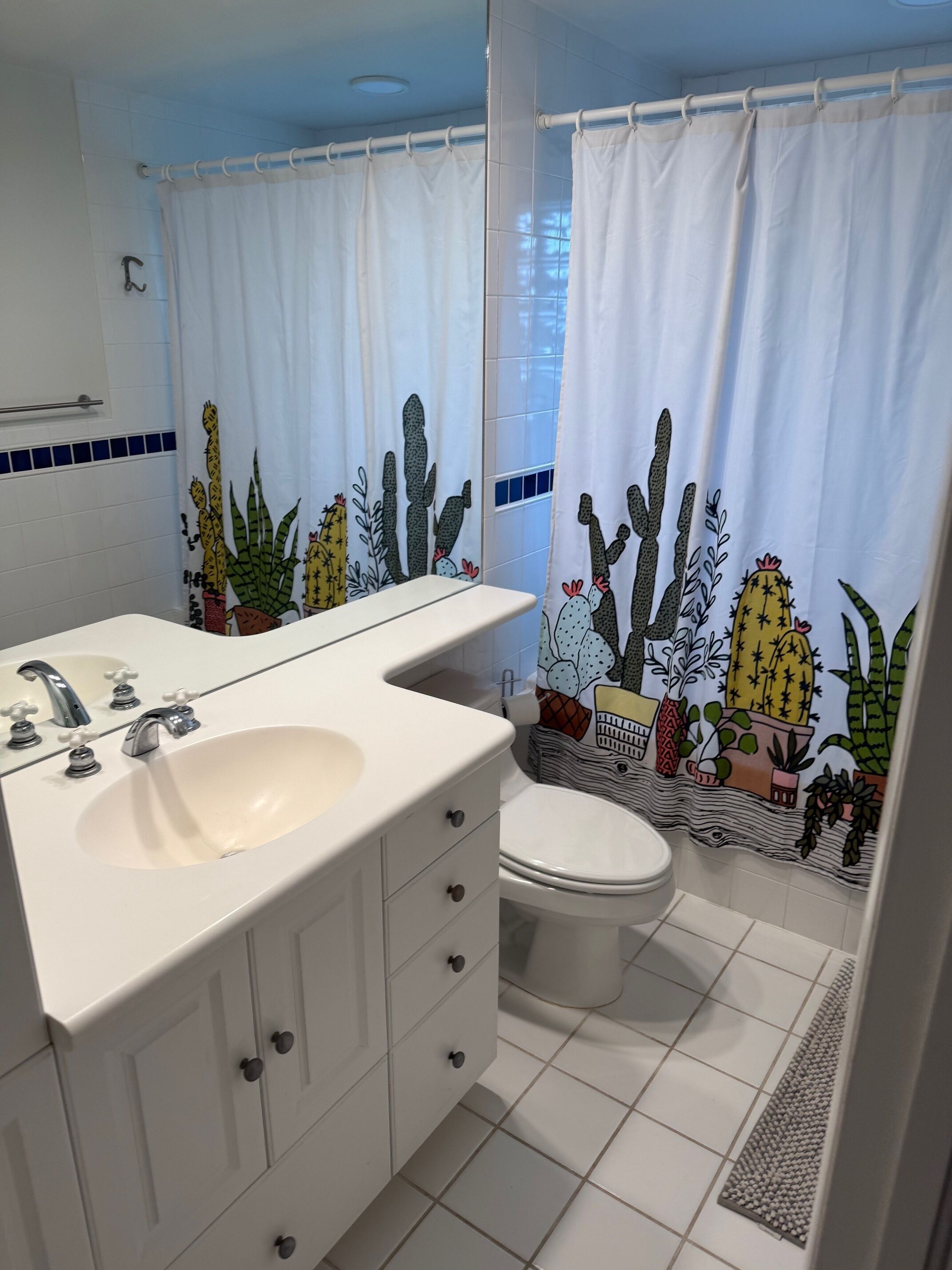 Une salle de bain avec un lavabo blanc, des toilettes et un rideau de douche orné de motifs de cactus.
