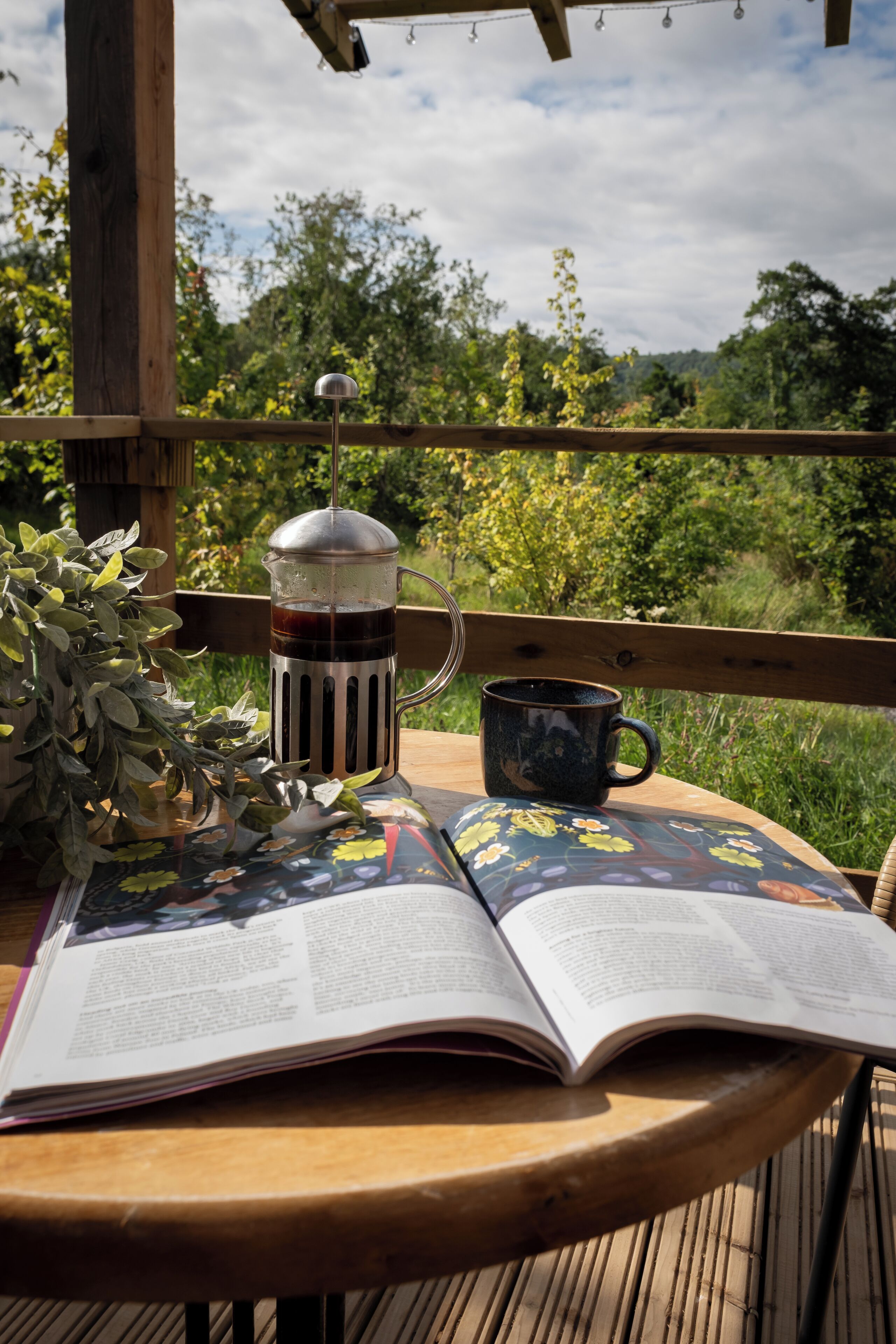Un libro abierto sobre una mesa de madera, con una cafetera y una taza cerca.