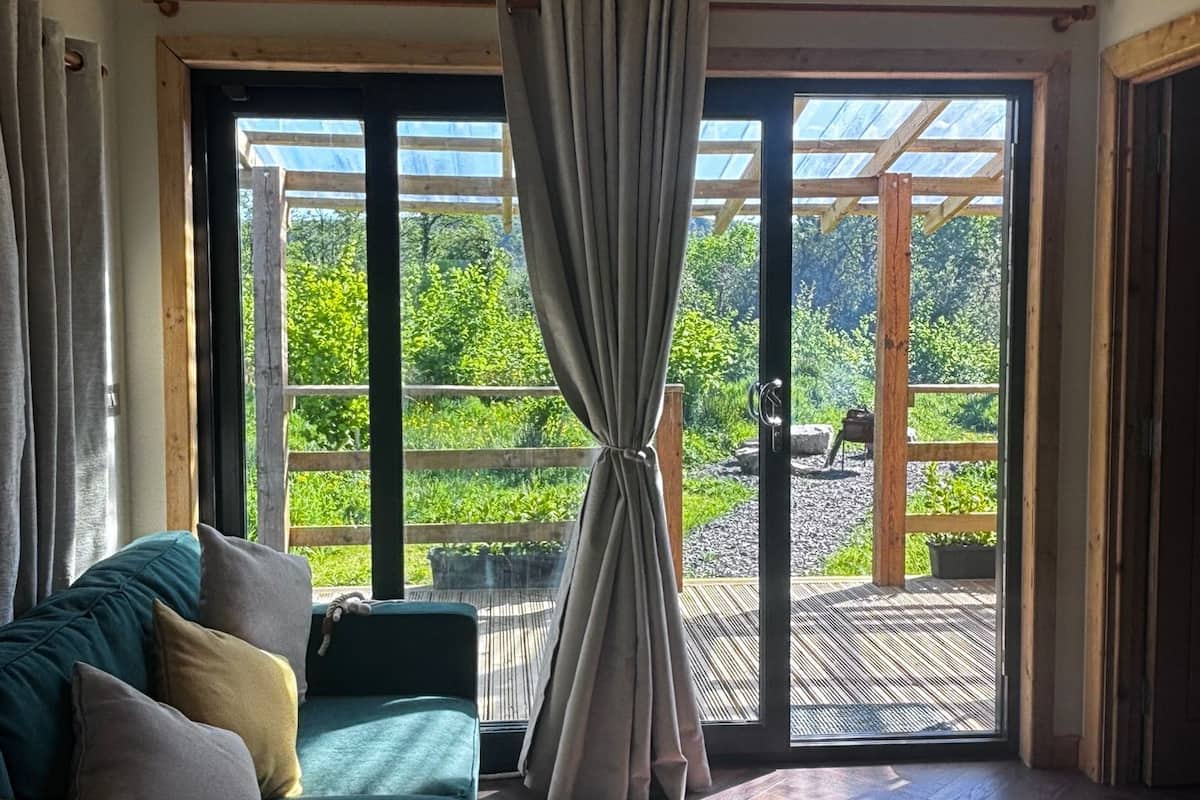 A room with a sofa, a large sliding glass door leading to an outdoor deck, and a view of greenery.