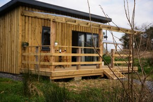 A wooden cabin with a deck, large windows, and a small porch.