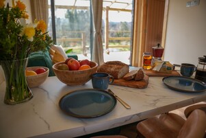 Una encimera de cocina con un cuenco de fruta, una hogaza de pan, un plato, una taza y un tarro de miel.