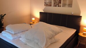 A neatly made bed with white linens and pillows, a dark headboard, and two bedside lamps. - Home Sweet Home - Feel-good vacation home (Cuxhaven)