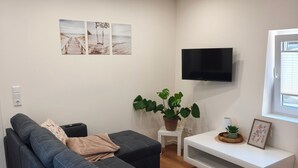 A modern living room with a sectional sofa, a flat-screen TV, a potted plant, and artwork on the wall. - Home Sweet Home - Feel-good vacation home (Cuxhaven)