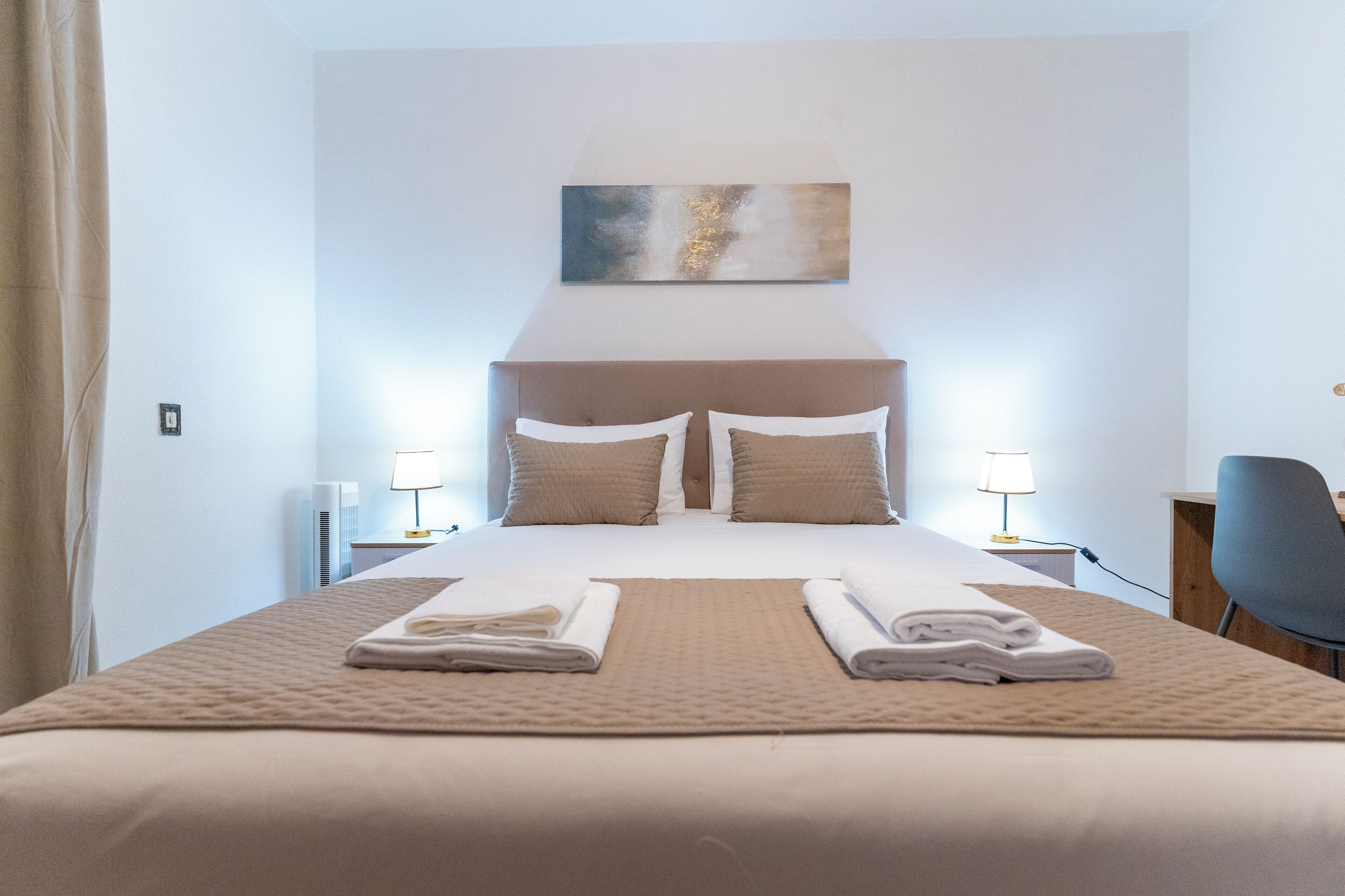 A neatly made bed with towels, a headboard, and a painting above it.