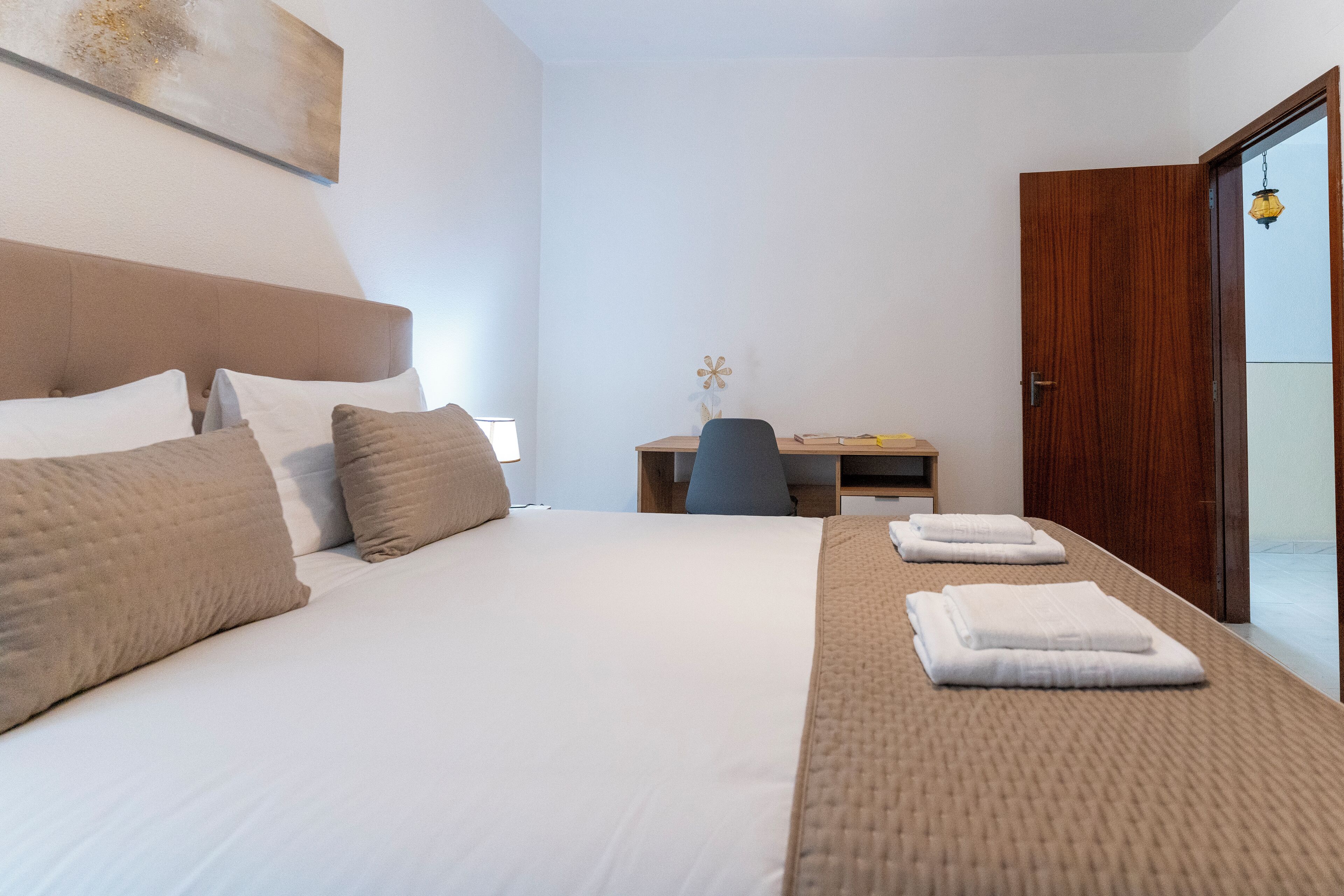 A hotel room with a large bed, a desk, and a door leading to a balcony.