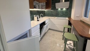 A compact kitchen with white cabinets, a built-in oven, and a green marble backsplash. There are two green stools at the counter. - African House Peschici (Peschici)