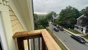 A residential street view from a balcony with a wooden railing, houses, and cars on the road. - Wolfville DT • Modern 3BR • 1.5 Bath Suite Seaview (Wolfville)