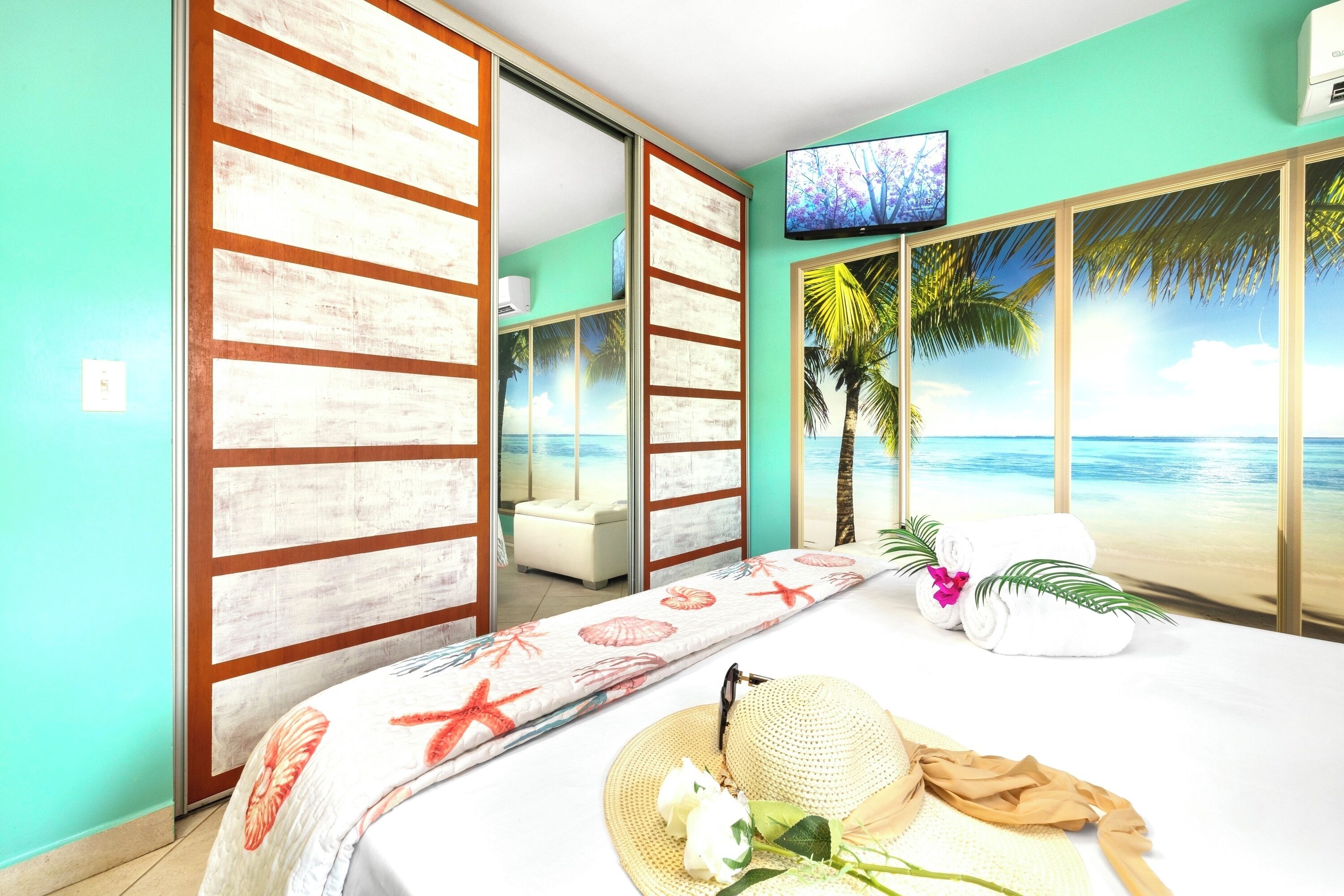 Een kamer met een bed, een televisie, een schuifdeur met uitzicht op het strand en een witte bank.