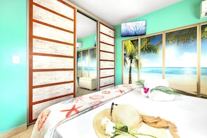 A room with a bed, a TV, a sliding door with a beach view, and a white sofa. - Perfect 2-bedroom/2-bathroom condo with AC in Palm Beach. (Noord)