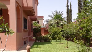 A courtyard with a well-maintained lawn, a large decorative vase, and a building with arches and a balcony. - Large villa with private garden and pool, ideal for families and friends. (Marrakech)