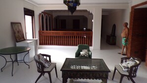 A spacious living area with a high ceiling, a green round table, two chairs, a small wooden table, and a statue of a man. - Large villa with private garden and pool, ideal for families and friends. (Marrakech)
