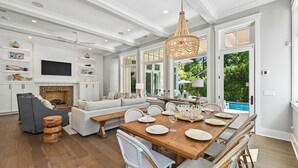 Amplia sala de estar con chimenea, una mesa de comedor para seis personas y un gran ventanal con vista a una piscina.