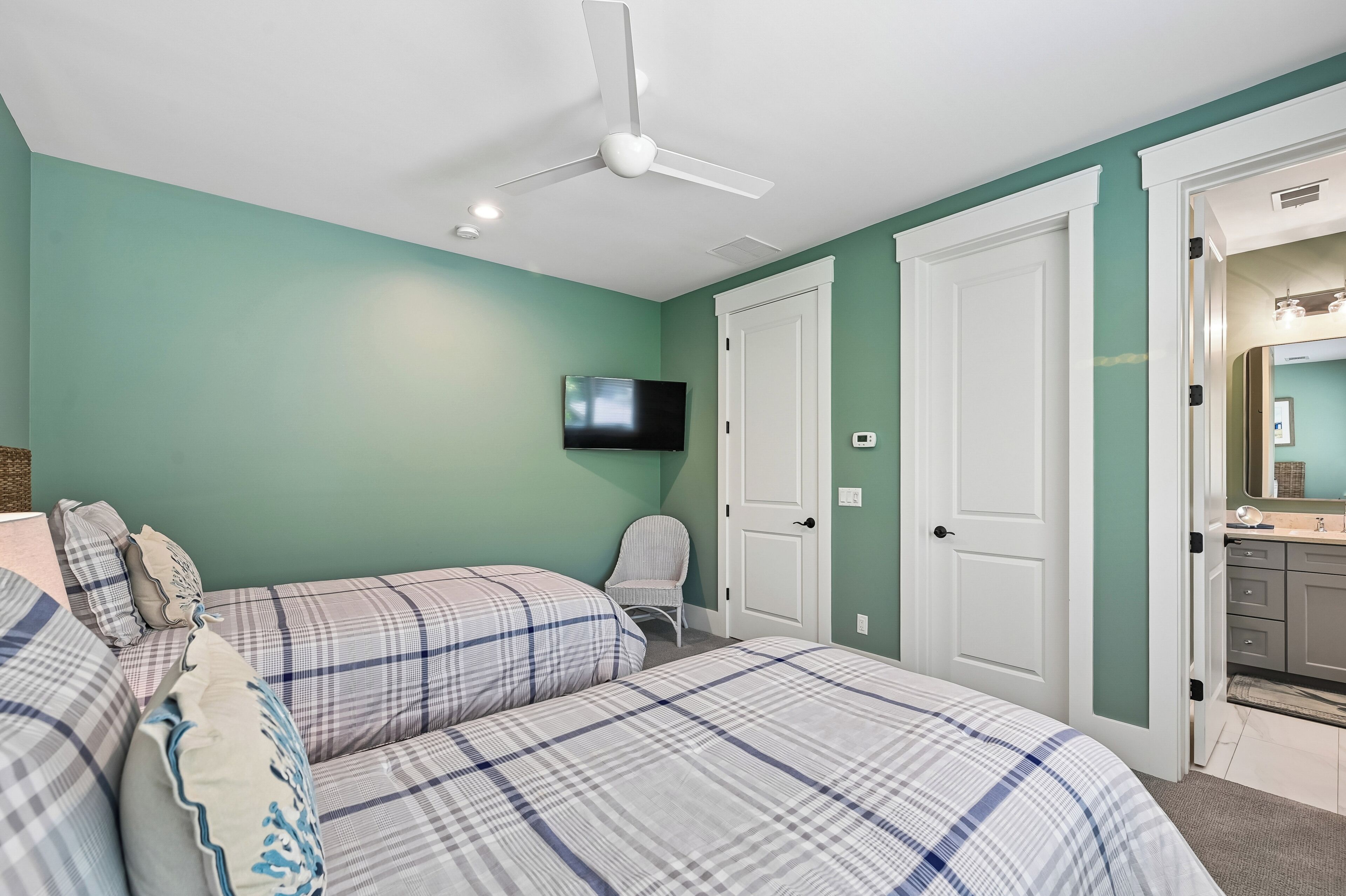 Quarto com duas camas, um ventilador de teto, uma TV e uma porta que dá para um banheiro.