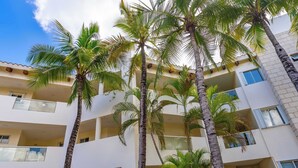 Un immeuble à plusieurs étages, doté de balcons, de palmiers et surplombant un ciel dégagé.