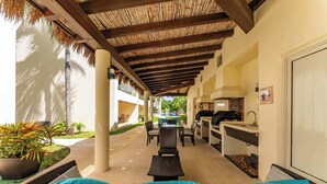 Une terrasse extérieure avec des meubles en osier, un barbecue et une vue sur la piscine.