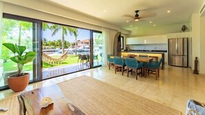 Una cucina moderna con zona pranzo, ampie finestre e vista su una piscina e palme.