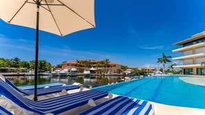 Un’area piscina con lettini e ombrelloni, un porto turistico con imbarcazioni e un edificio con tetto rosso.