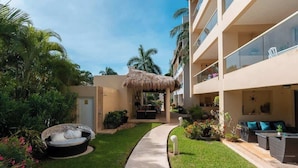 A hotel courtyard with a thatched-roof seating area, a pathway, and lush greenery. - Family escape with pool & beach acces (Puerto Aventuras)