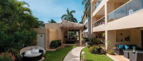 A hotel courtyard with a thatched-roof seating area, a pathway, and lush greenery.