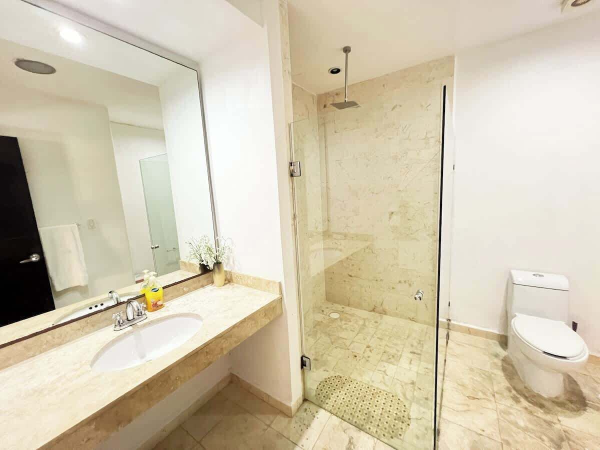Un baño moderno con ducha envuelta en vidrio, lavamanos con espejo y retrete.