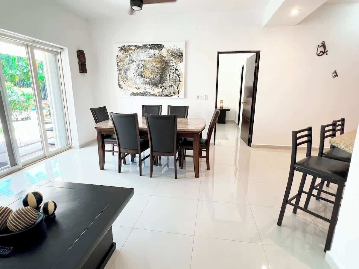 A modern dining area with a large table and chairs, a black coffee table, and a view of the outdoors through large windows.