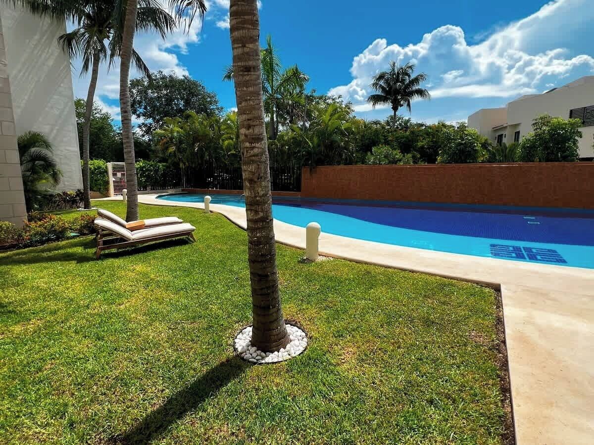 Una piscina rodeada de césped cuidado, palmeras y un cielo azul despejado.