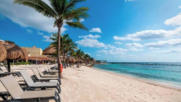 A beach with lounge chairs and palm trees, a clear sky, and a calm sea. - Family escape with pool & beach acces (Puerto Aventuras)