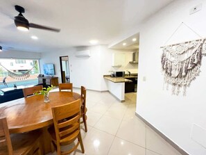 A modern kitchen with a microwave, stove, and sink. There is a dining area with a wooden table and chairs. - Beachside Condo w/ Private Terrace & 2 Pools (Puerto Aventuras)