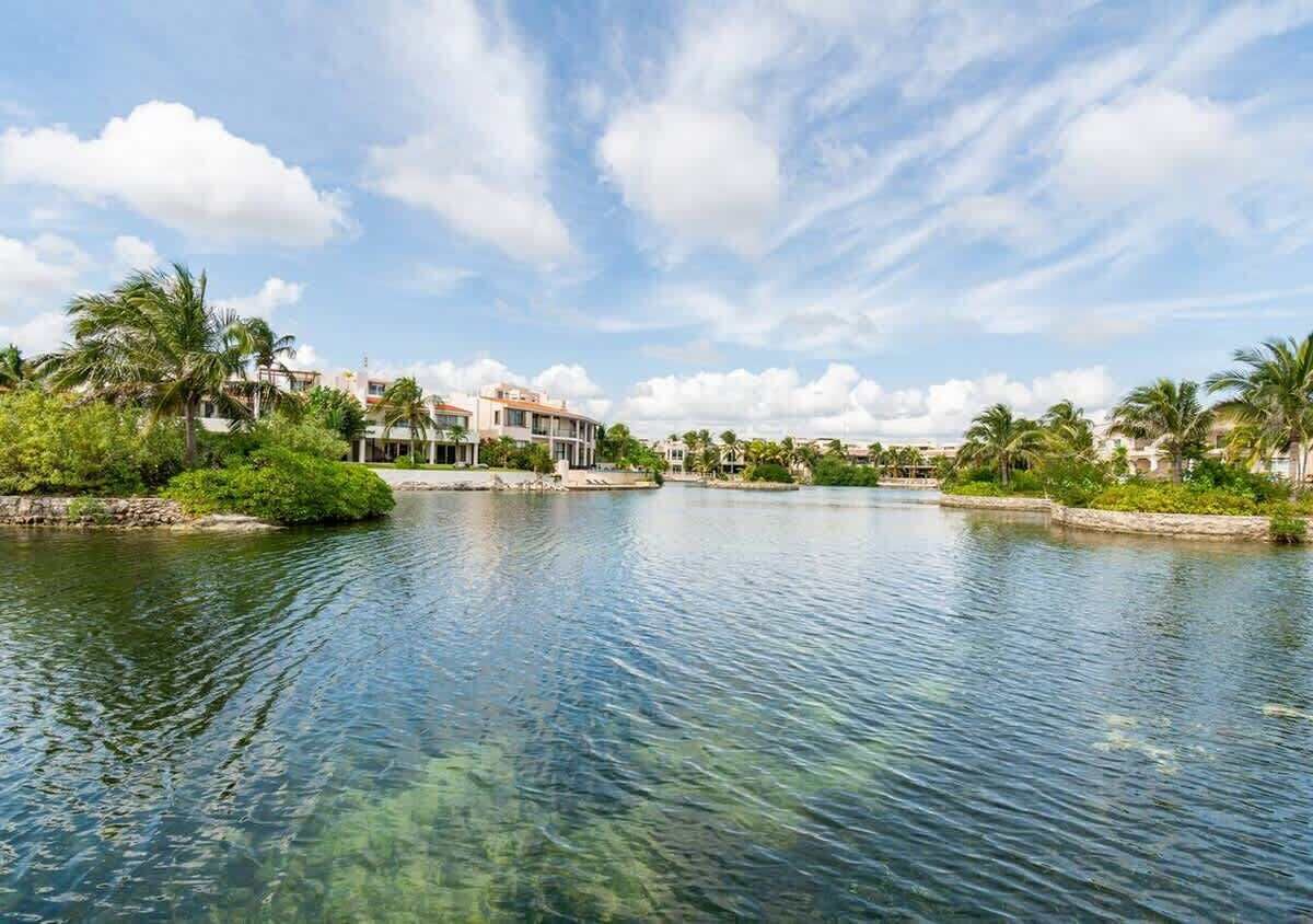 Een hotel aan het water met een rustige rivier, palmbomen en een heldere lucht.