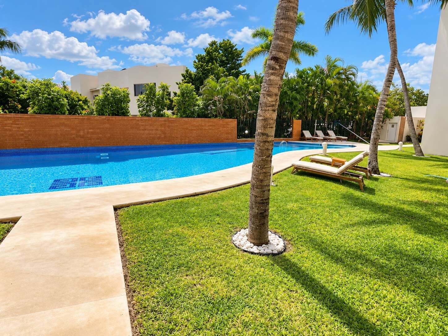 Una piscina con agua cristalina azul, rodeada de césped cuidado y palmeras.