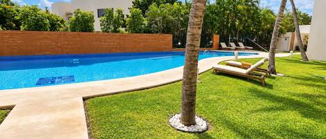 Una piscina con agua cristalina azul, rodeada de césped cuidado y palmeras.
