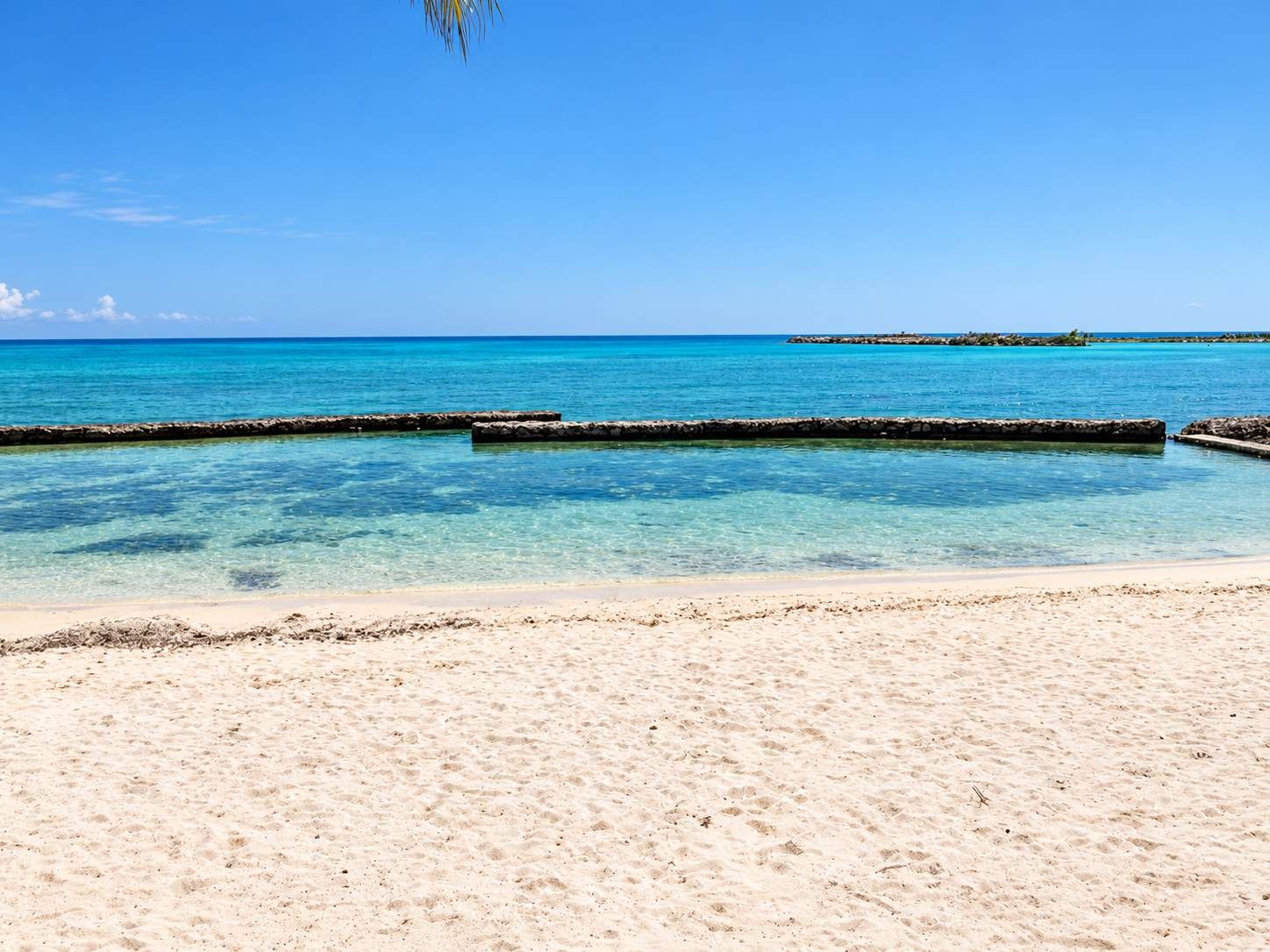 A beach with clear turquoise water, a sandy shore, and a distant island.
