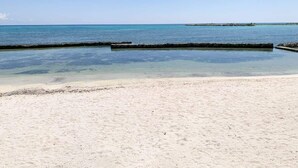 A beach with clear water, a sandy shore, and a distant pier. - Beachside Condo w/ Private Terrace & 2 Pools (Puerto Aventuras)